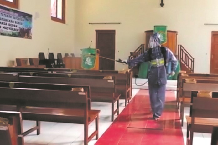 Petugas melakukan sterilisasi dengan menyemprotkan disinfektan di dalam gereja. (Istimewa)