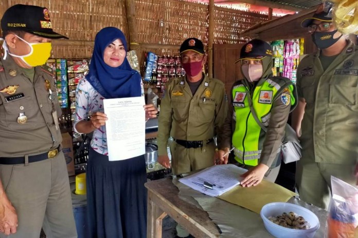 Petugas Satpol PP Pemkab Demak melakukan operasi yustisi terhadap warung tepi jalan Pantura  lingkar selatan Kota Demak. Seorang penjaga warung berkerudung menujukkan lembaran kertas berisi tata tertib warung.  (Wahib Pribadi/Jawa Pos Radar Semarang)