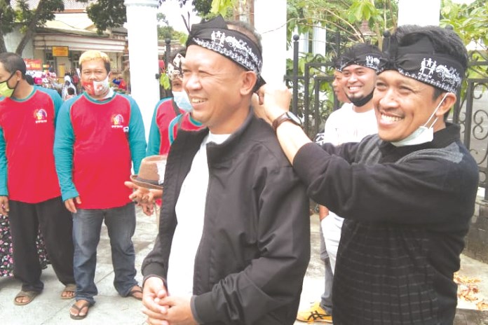 Bupati Wonosobo terpilih Afif Nurhidayat saat tengah memakaikan oleh-oleh khas Wonosobo, iket saba kepada pembina PPMAW, Idham Kholid di Pasar Mingguan. (Istimewa)
