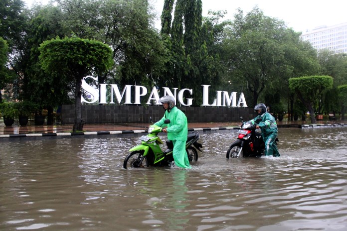 Dua pengendara motor menuntun kendaraannya saat melewati genangan banjir di kawasan Simpang Lima, Semarang. (BASKORO SEPTIADI/JAWA POS RADAR SEMARANG)