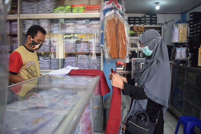 Pembeli memilihkan seragam untuk anaknya yang baru memasuki SD di toko HA Kadir, Jalan Kauman, Semarang, Minggu (21/2/2021). (TITIS ANIS FAUZIYAH/JAWA POS RADAR SEMARANG)