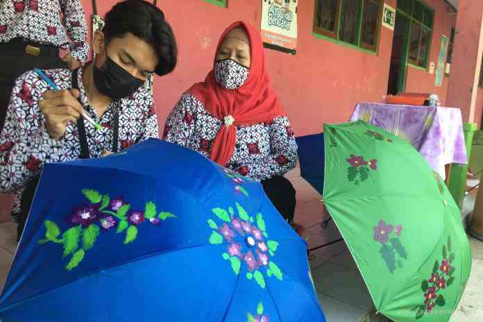 PIAWAI: Desta Eka Nanda Siswa SLB Swadaya Kaliwungu didampingi gurunya saat melukis di atas payung.(BUDI SETIYAWAN/ JAWA POS RADAR SEMARANG)