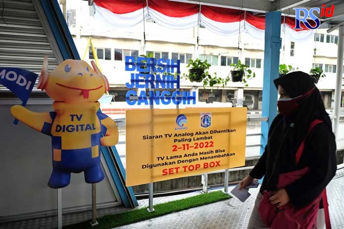 Calon penumpang TransJakarta melintas didepan Iklan Layanan Masyarakat untuk program Migrasi TV Digital di Halte Harmoni, Jakarta Pusat, Jumat, 20 Agustus 2021.