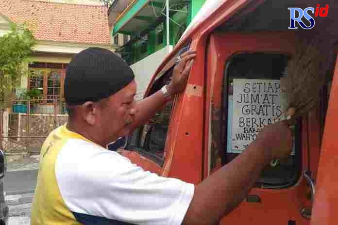 Rusmadi saat menempel tulisan gratis setiap Jumat di kaca pintu angkotnya. (M HARIYANTO/JAWA POS RADAR SEMARANG)