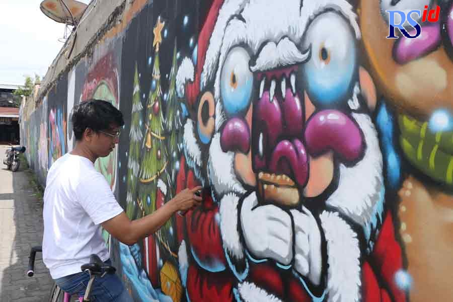 Duduk di atas sepedanya, Woky menggambar mural Natal di dinding Jalan Jendral Sudirman, Karangayu, Kota Semarang, Minggu  (12/12). (NUR CHAMIM/JAWA POS RADAR SEMARANG)