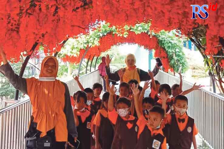 Bunga kuku macan berwarna merah cerah bermekaran. Pengunjung kebun berfoto bersama di bawah bunga kuku macan yang menggantung.  (Istimewa)