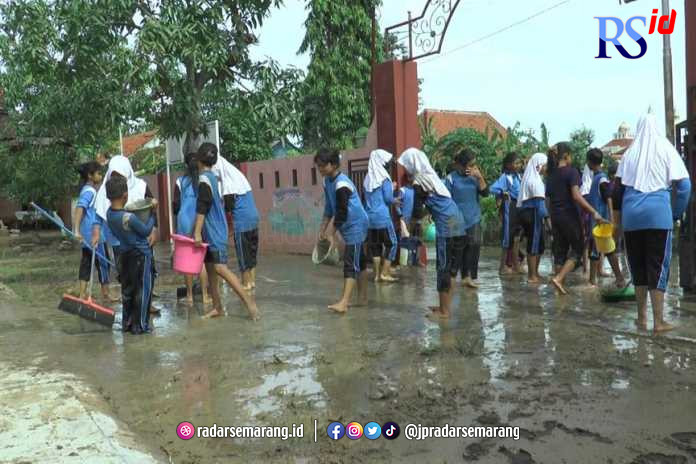 Para siswa SD Negeri 1 Kebonadem Brangsong bergotong royong membersihkan lumpur di halaman sekolah, Senin (2/1/2023). (BUDI SETIYAWAN/JAWA POS RADAR SEMARANG)