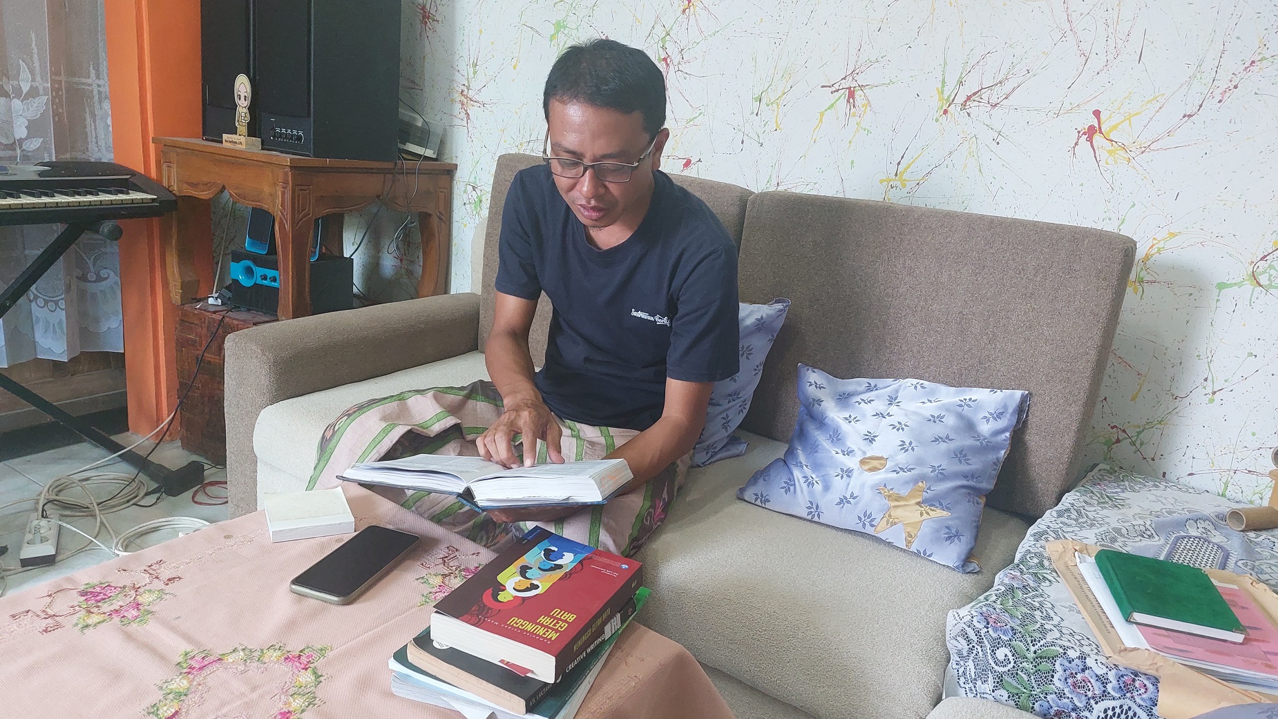 Mudhar CH membaca buku di rumahnya yang beralamat di Kelurahan Karang Dalem, Kecamatan Kota Sampang, Rabu (5/7). (JUNAIDI PONDIYANTO/JPRM)