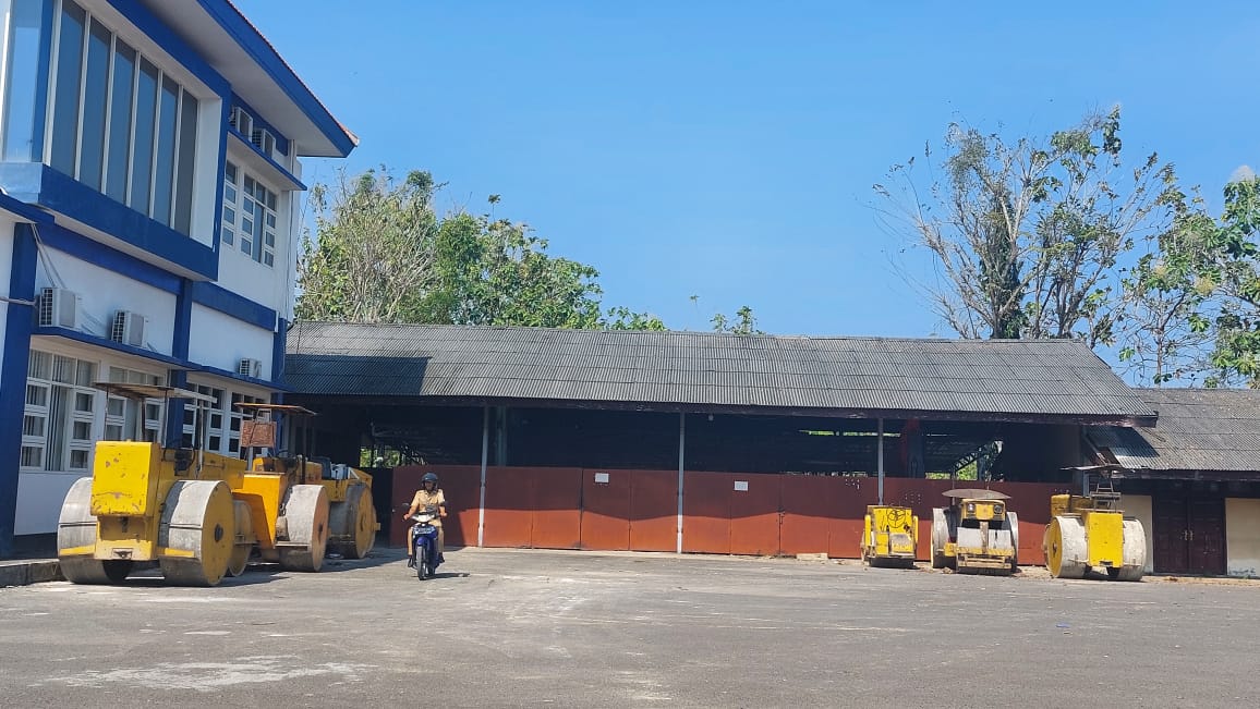 ALAT BERAT: Salah seorang pegawai melintas di sekitar mesin gilas yang terparkir di Dinas PUPR. (JUNAIDI PONDIYANTO/JPRM)