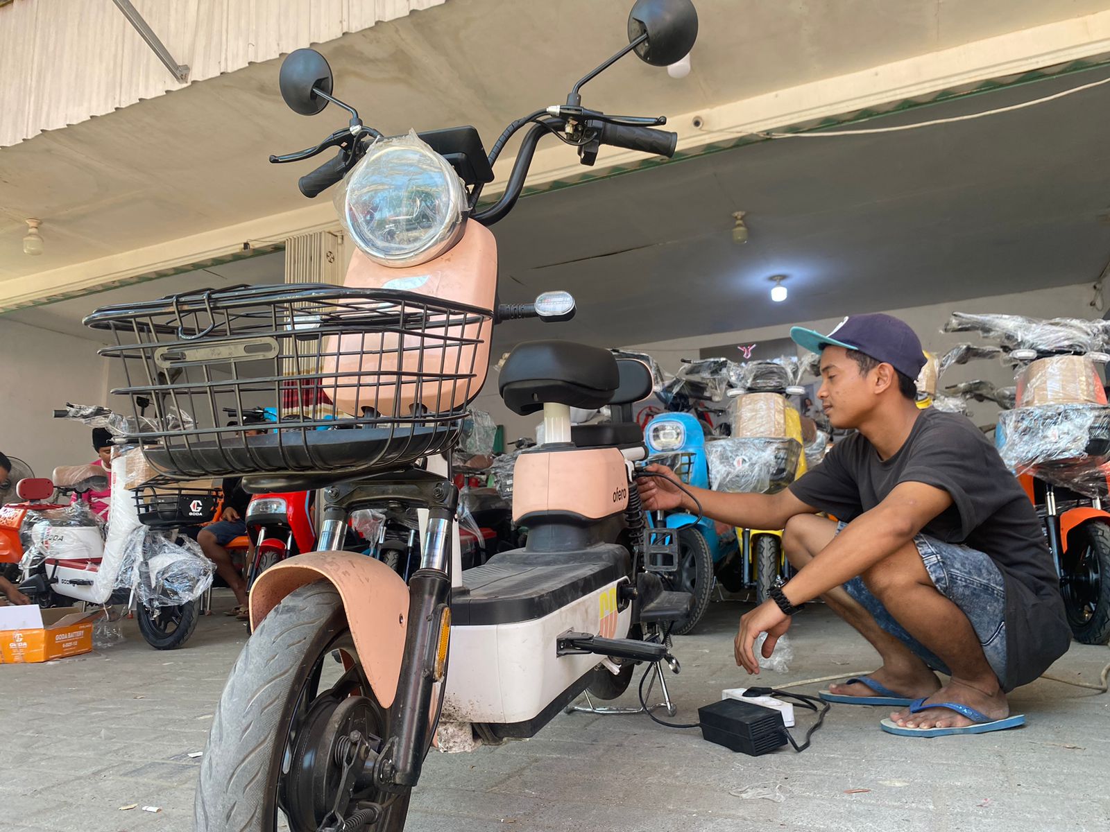 Mekanik sepeda listrik Mohamad Nashrullah memasang aki dan charging di salah satu showroom di Pamekasan, Kamis (3/8).