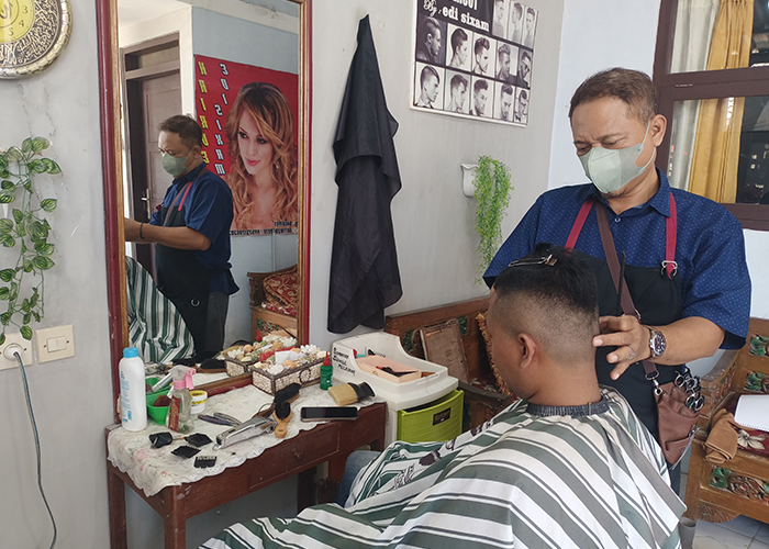 FOKUS: Edi Sixam memotong rambut pelanggan di rumahnya yang berlokasi di Perumahan Pendopo Agung Residence, Desa/Kecamatan Batuan, Sumenep.