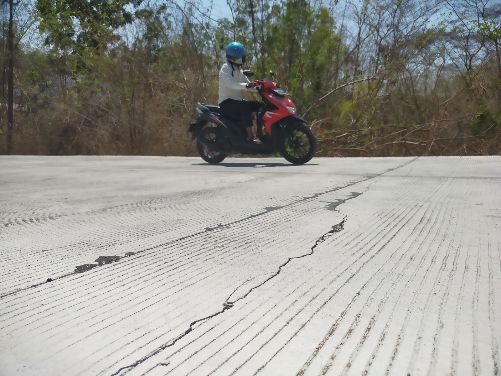 TERIK: Warga melintasi jalan beton yang mengalami keretakan pada kegiatan pemeliharaan berkala atau peningkatan struktur Jalan Kotah&ndash;Tambelangan, Minggu (24/9). (ANIS BILLAH/JPRM)