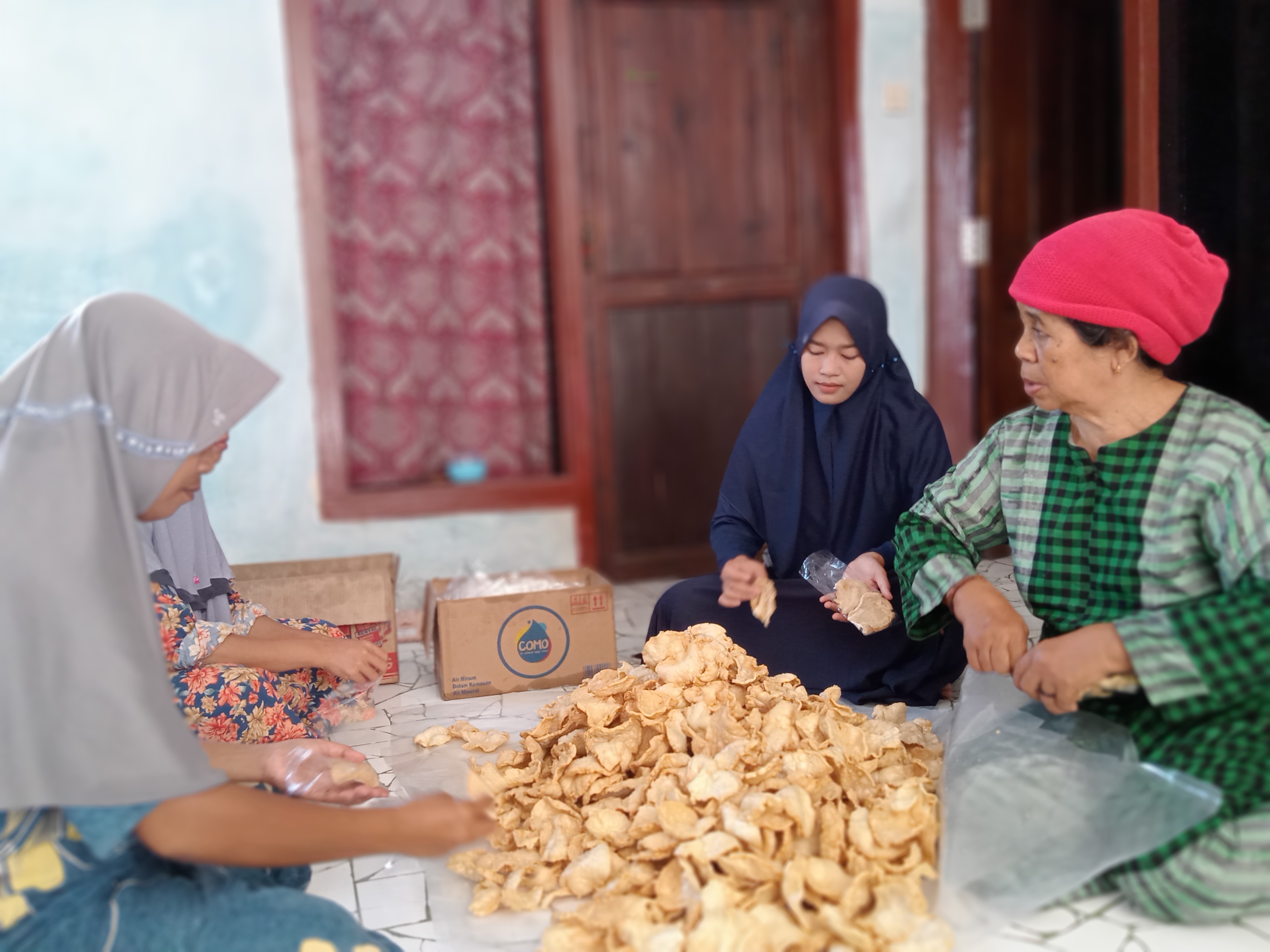 TELATEN: Anis Khofifatun Nafilah (kerudung navy) mendampingi pekerja saat mengemas kerupuk Sabtu (21/10) di Desa Tanjung, Kecamatan Pademawu, Pamekasan. (UBAIDILLAHIR RA&rsquo;IE/JPRM)