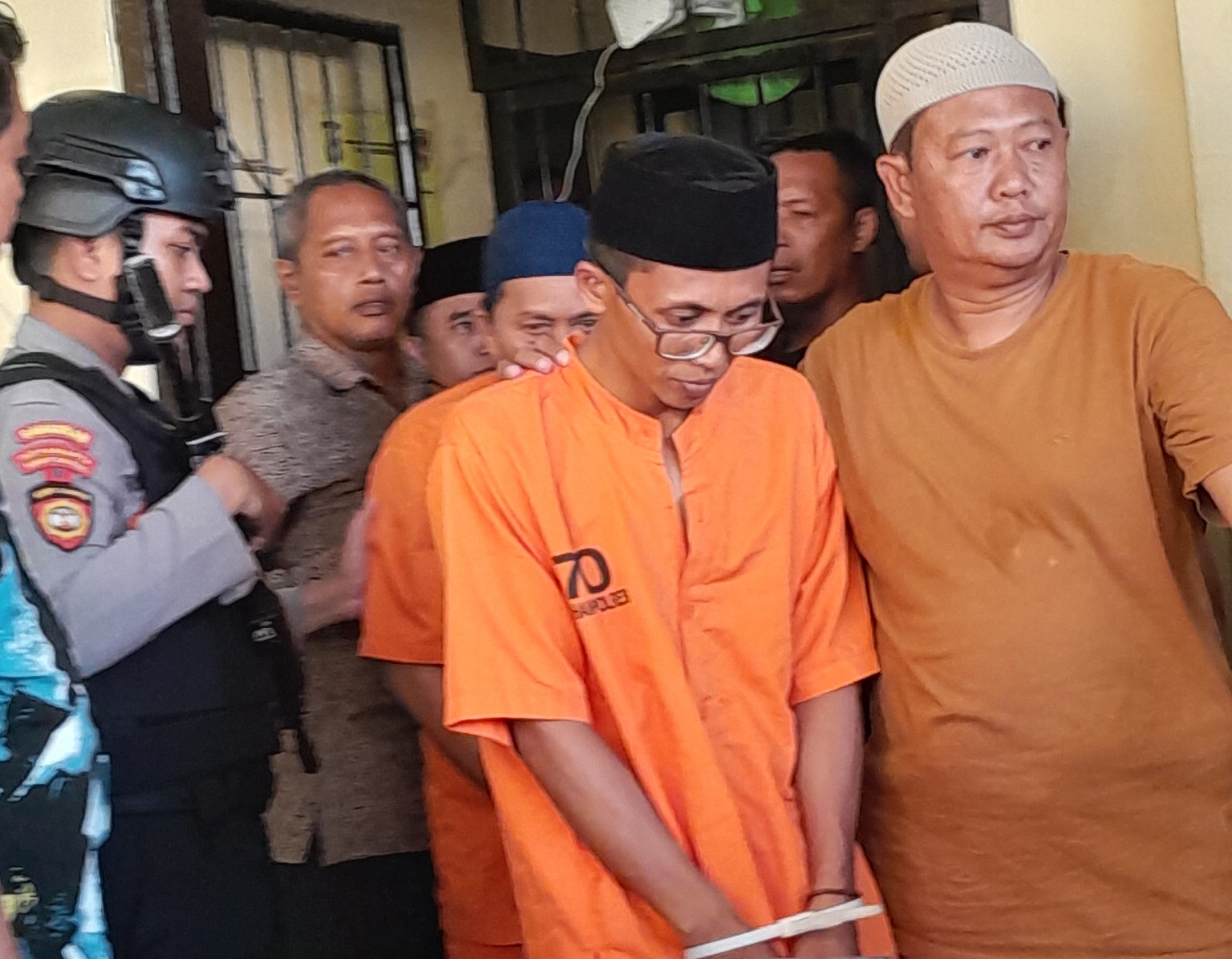 MENUNDUK: Polisi mengawal Karimullah (berkaca mata) dari sel tahanan menuju halaman depan Mapolres Sumenep, Jumat (20/10). (MOH. BUSRI/JPRM)