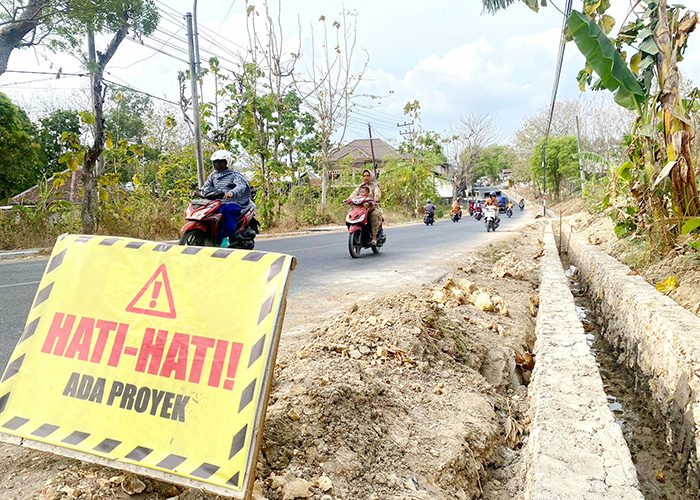 BELUM TUNTAS: Pengendara sepeda motor melintas di dekat proyek drainase yang ada di Desa Larangan Badung, Kecamatan Palengaan. (MOH. JUNAIDI/JPRM)