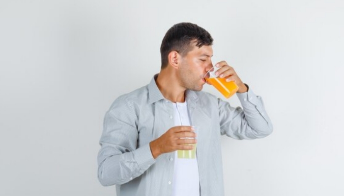 Orang sedang minum jus jeruk untuk menjaga kesehatan saat musim hujan