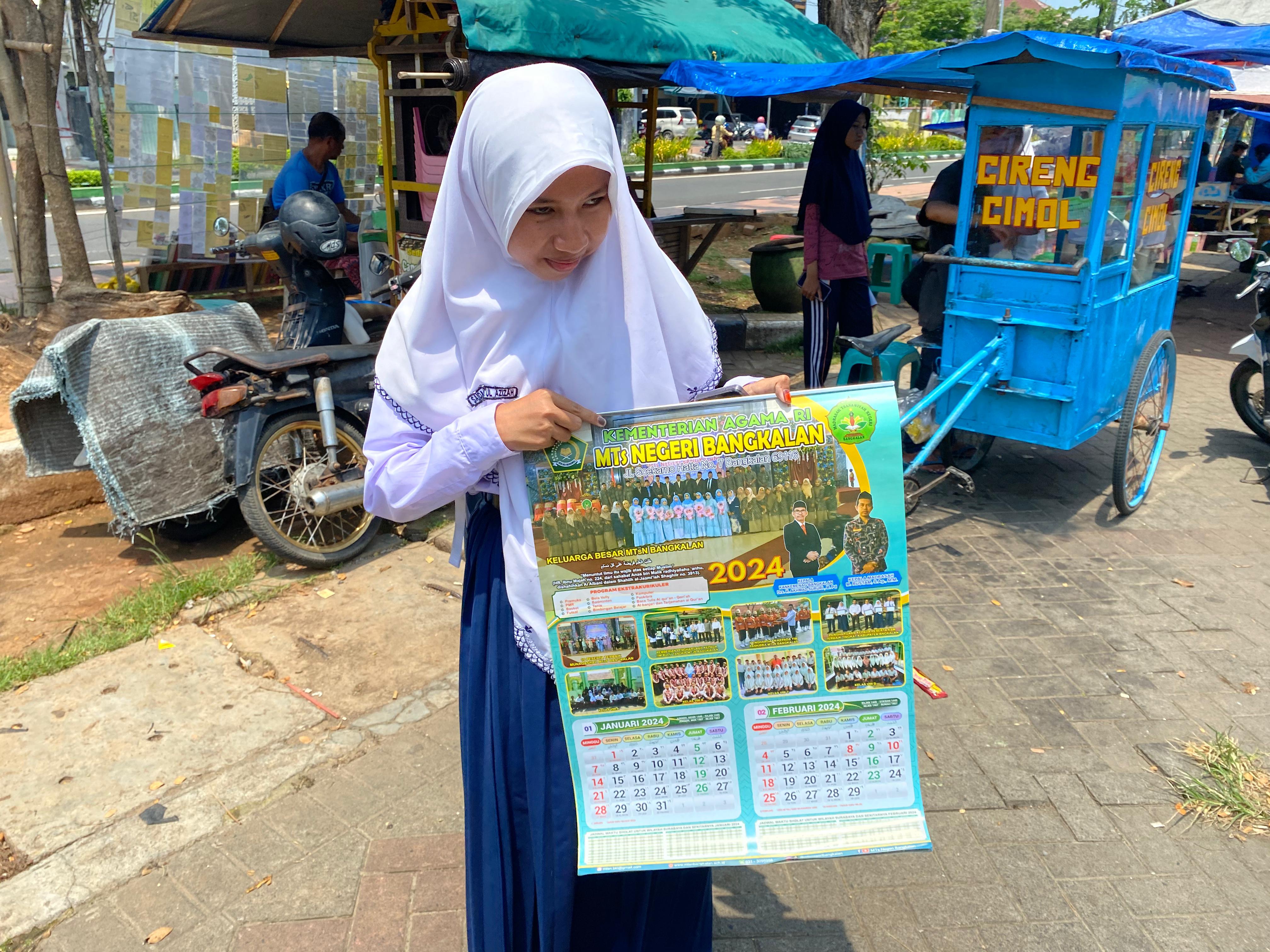 TIDAK GRATIS: Seorang siswi memegang kalender di sekitar MTsN Bangkalan, Senin (11/12). (AYU LATIFAH/JPRM)