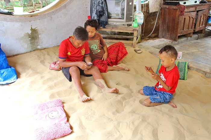 BERSANTAI: Anak-anak usia sekolah menikmati hari libur sambil main gadget di hamparan pasir putih di halaman rumah warga Dusun Pasaran, Desa Legung Timur, Batang-Batang, Sumenep. (HERIVIYA YUVI/JPRM)