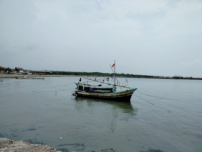 SANTAI: Seorang nelayan di Desa Branta Pesisir, Kecamatan Tlanakan, Pamekasan, sedang membersihkan perahunya Minggu (7/1). (LAILIYATUN NURIYAH/JPRM)