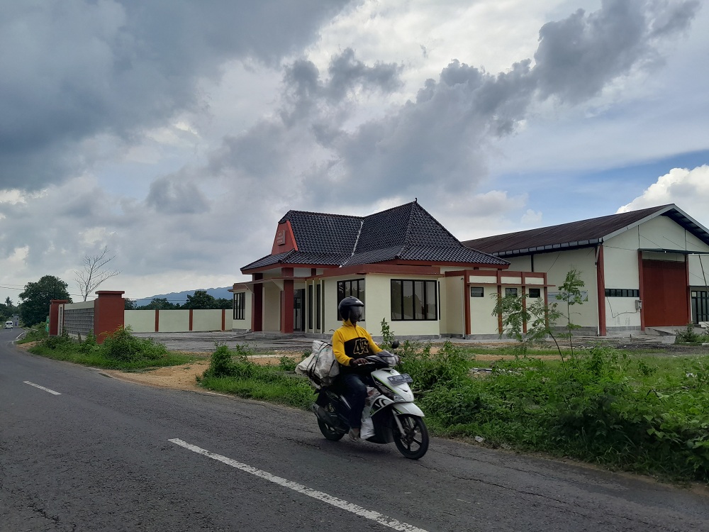 TELAN BELASAN MILIAR: Pengendara motor melintas di Jalan Raya Guluk-Guluk, depan gedung KIHT yang pembangunannya belum tuntas hingga, Minggu (28/1). (MOH. BUSRI/JPRM)