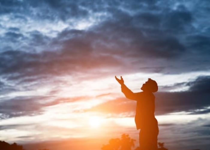 Orang sedang berdoa kepada Tuhan dibawah langit senja.