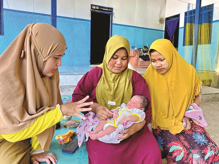 SEHAT: Bidan Desa Sejati Yuliani (kiri) menghibur Amira Hilyatun Nisak yang digendong dukun bayi Halisa di samping Subaidah (kanan) Selasa (30/1). (ANIS BILLAH/JPRM)