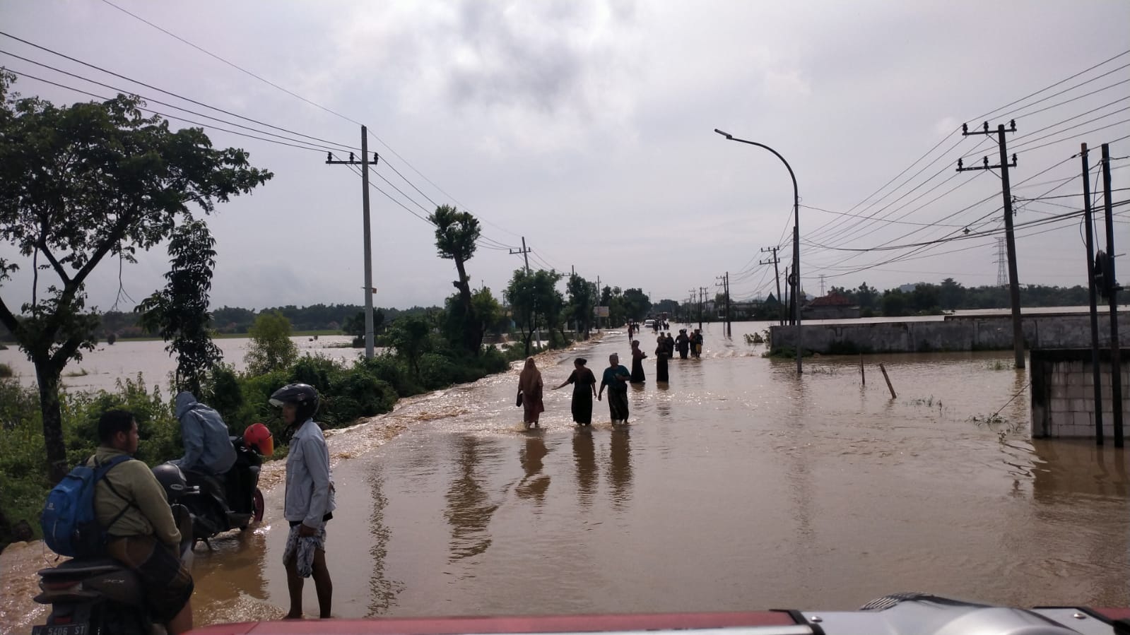 JALUR UTAMA TERGANGGU: Pengendara motor berhenti di jalan nasional Kecamatan Jrengik, Sampang, akibat luapan air, Selasa (12/3). (BPBD SAMPANG UNTUK JPRM)