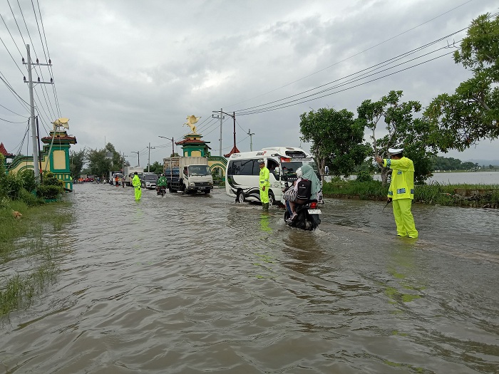 HARAP PELAN: Personel Satlantas Polres Sumenep menertibkan arus lalu lintas di lokasi genangan air di Desa Patean, Kecamatan Batuan, Kamis (14/3). (MOHAMAD ERWIN MAULIDIN M/JPRM)