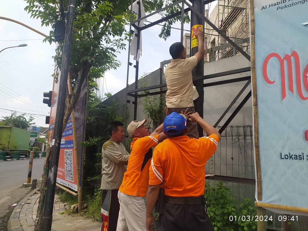 PELANGGARAN: Petugas Satpol PP dan Damkar Pamekasan memasang stiker kerangka APK yang tidak berizin di Jalan Trunojoyo, Kelurahan Patemon, Pamekasan.