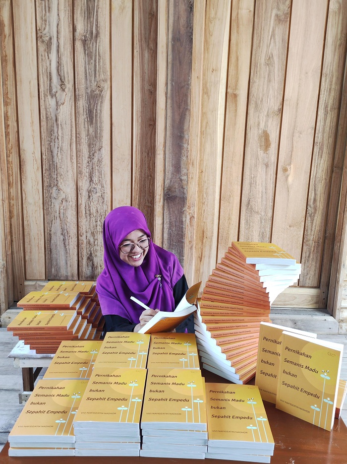 PENUH KARYA: Neng Vivi Nafidzatin Nadhor menandatangani buku Pernikahan Semanis Madu Bukan Sepahit Empedu hasil karyanya sebelum dikirim kepada pembaca. (VIVI NAFIDZATIN NADHOR UNTUK JPRM)