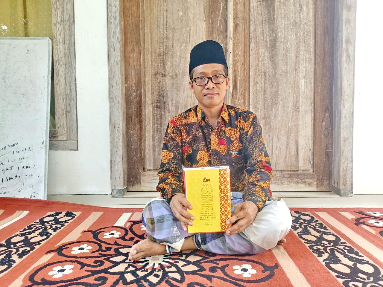 BERWAWASAN: Kiai A. Mufti Khazin memegang buku konsep Alfatih di kediamannya, Desa Rombiya Barat, Kecamatan Ganding, Sumenep, Jumat (5/4). (MOH. IQBAL/JPRM)