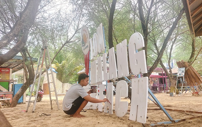 PEREMAJAAN: Pengelola mengecat plang di Pantai Lon Malang, Desa Bira Tengah, Kecamatan Sokobanah, Sampang, Sabtu (6/4). (JUNAIDI PONDIYANTO/JPRM)