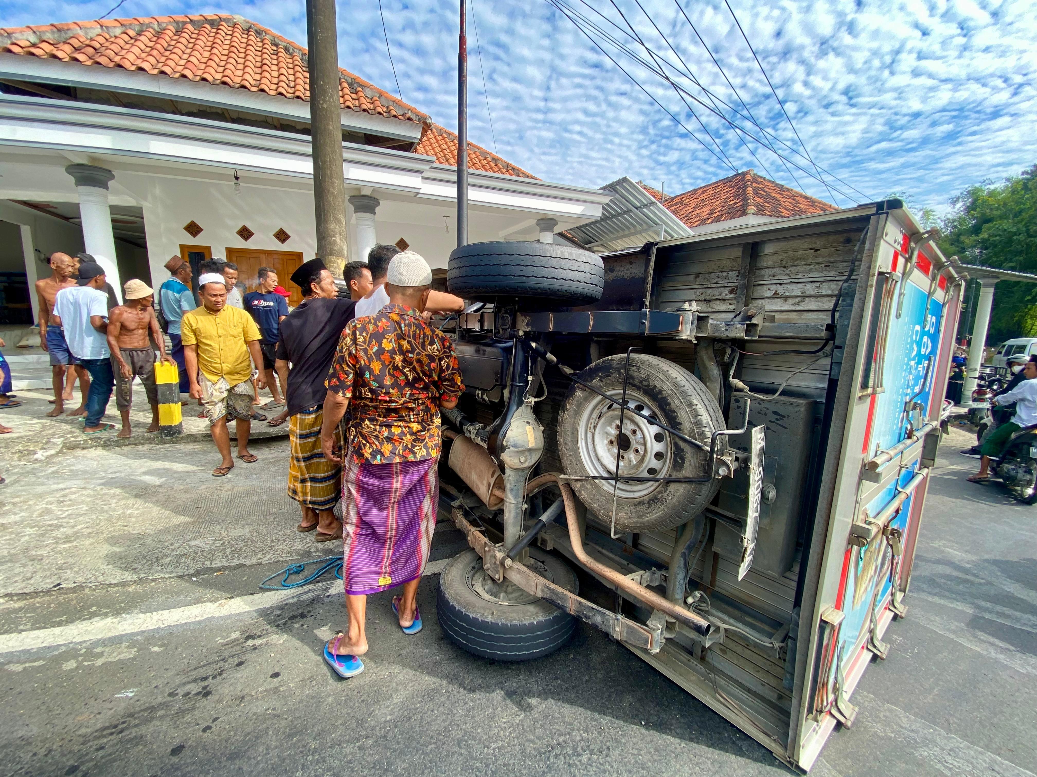 HATI-HATI: Warga berkerumun di lokasi mobil boks yang terguling di Desa Tampojung Guwa, Kecamatan Waru, Rabu (5/6). (MOH. IQBAL AFGANI/JPRM)