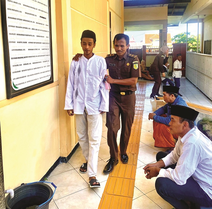 DIGIRING: Petugas tahanan Rifai mengarahkan terdakwa Angga Lukman Hakim ke ruang sidang PN Pamekasan Rabu (19/6). (MOH. IQBAL AFGANI/JPRM)