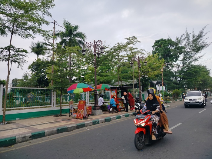 CARI PENGHASILAN: Pengendara motor melintas di dekat pedagang kaki lima yang sedang melayani pembeli Senin (24/6). (LAILIYATUN NURIYAH/JPRM)