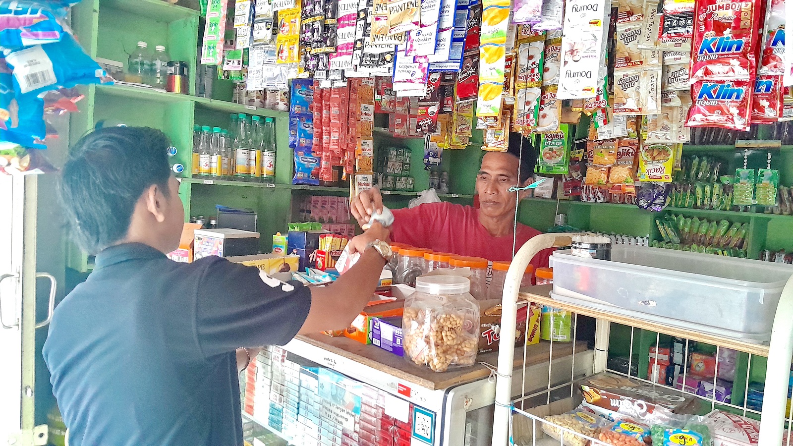 BERTRANSAKSI: Abd. Hafidz, penjaga toko kelontong di Kelurahan Pangeranan, Kecamatan/Kabupaten Bangkalan, sedang melayani warga yang membeli rokok, Kamis (9/5). (KHOLIL RAMLI/JPRM)