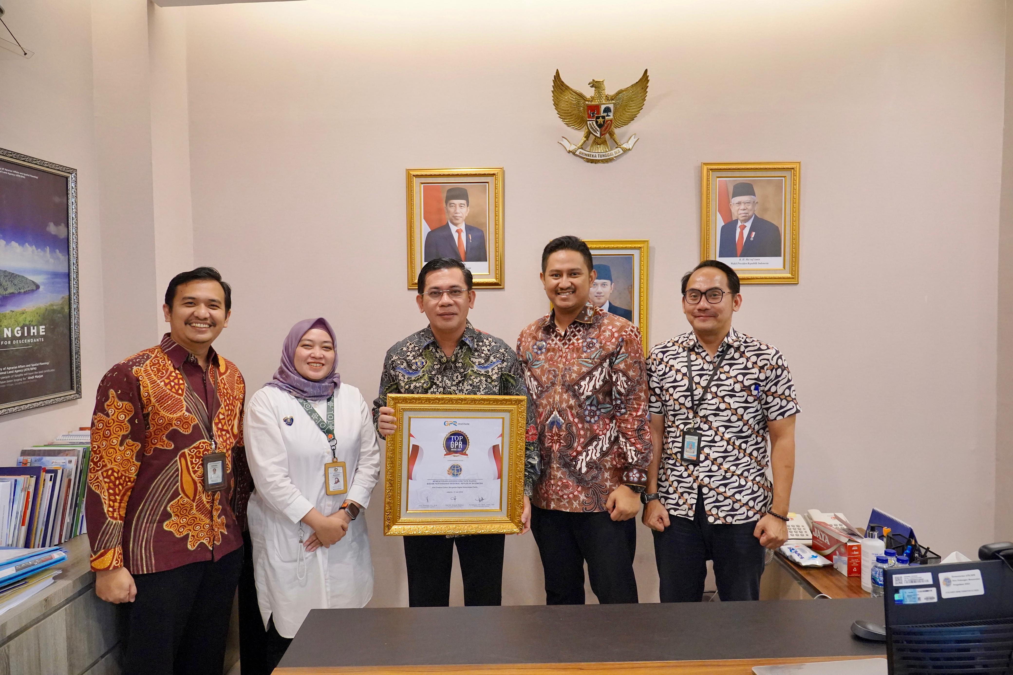 MEMBANGGAKAN: Kepala Biro Humas Kementerian ATR/BPN Harison Mocodompis (tengah) berpose usai menerima penghargaan di ruang kerjanya Rabu (17/7).