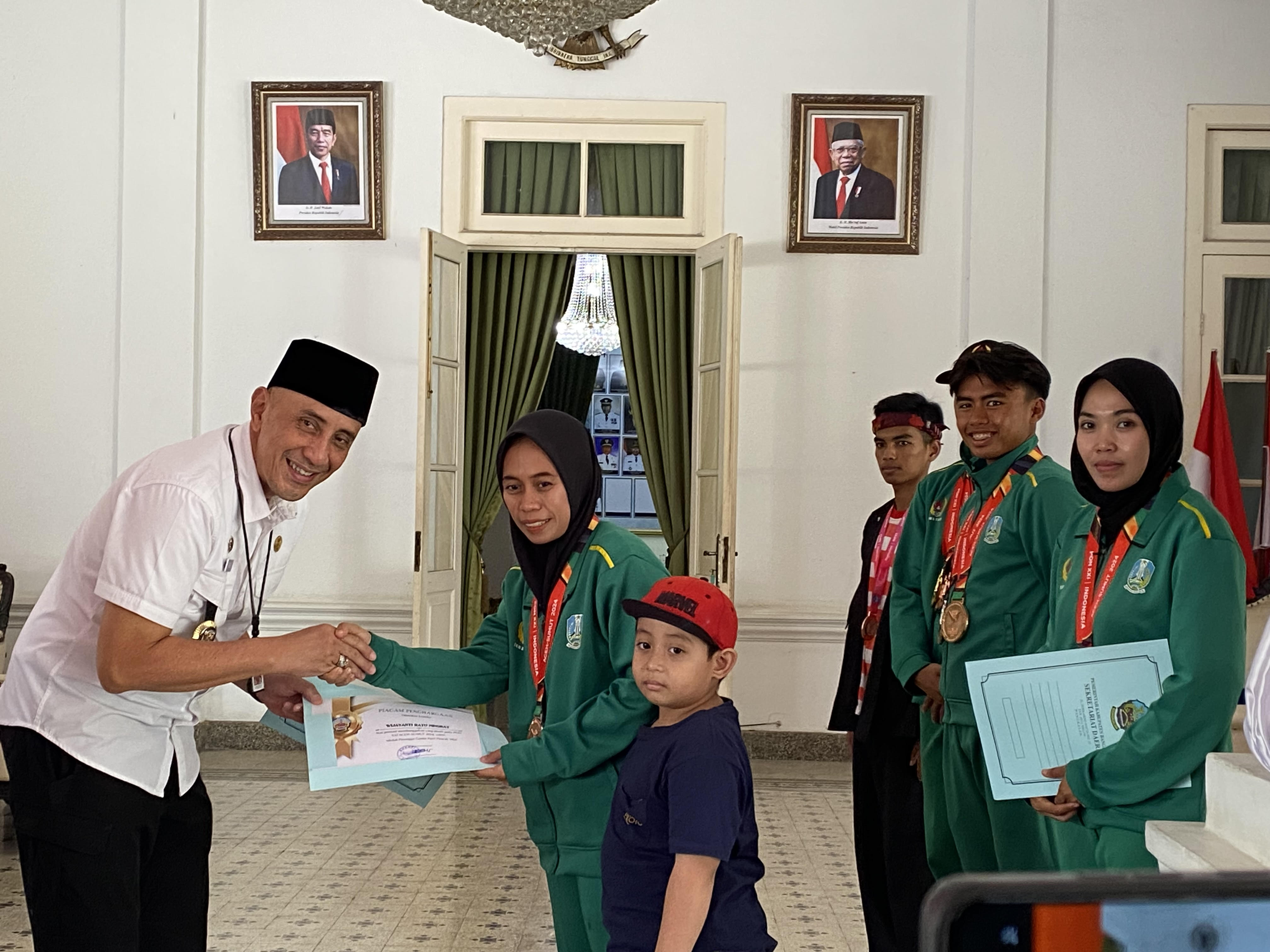 MEDALI PON XXI ACEH-SUMUT: Widjayanti Ratu Ningrat, atlet pencak silat seni ganda putri didampingi putranya saat menerima piagam penghargaan dari Pj Bupati Bangkalan di Pendopo Agung Rabu (25/9).