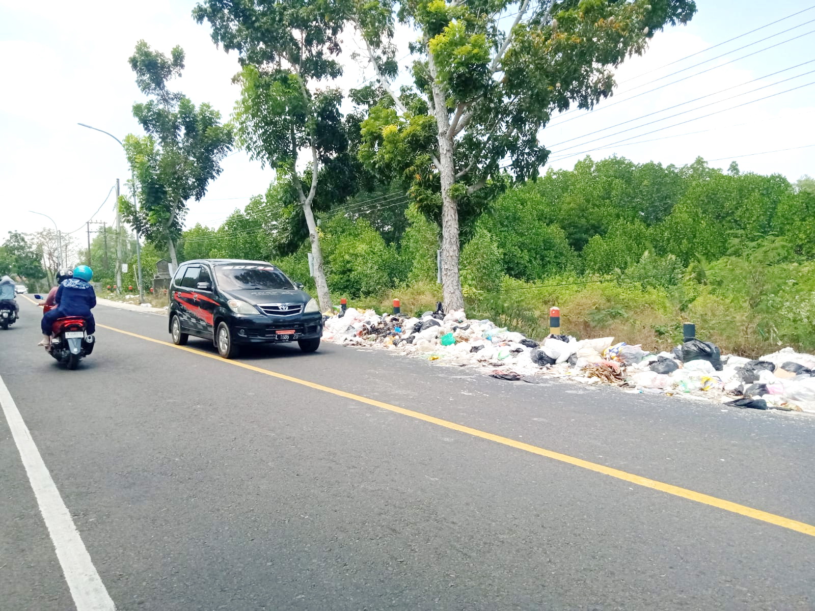 PERLU DIBERSIHKAN: Pengendara melintas di jalan dekat tumpukan sampah yang berpotensi menjadi tempat berkembangnya nyamuk Aedes aegypti, Rabu (21/8). (IMAMUDIN/JPRM)