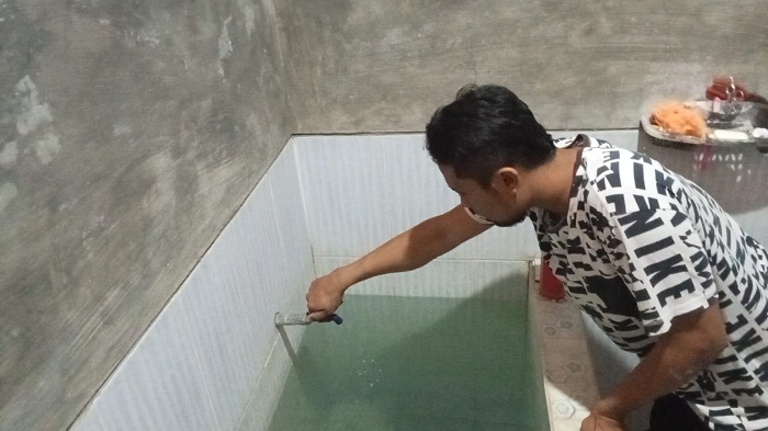 BAU TIDAK SEDAP: Pelanggan Perumdam Trunojoyo Darus Salam melihat kondisi air di rumahnya Kelurahan Polagan, Kecamatan Sampang, Senin (7/10). (DARUS SALAM UNTUK JPRM)