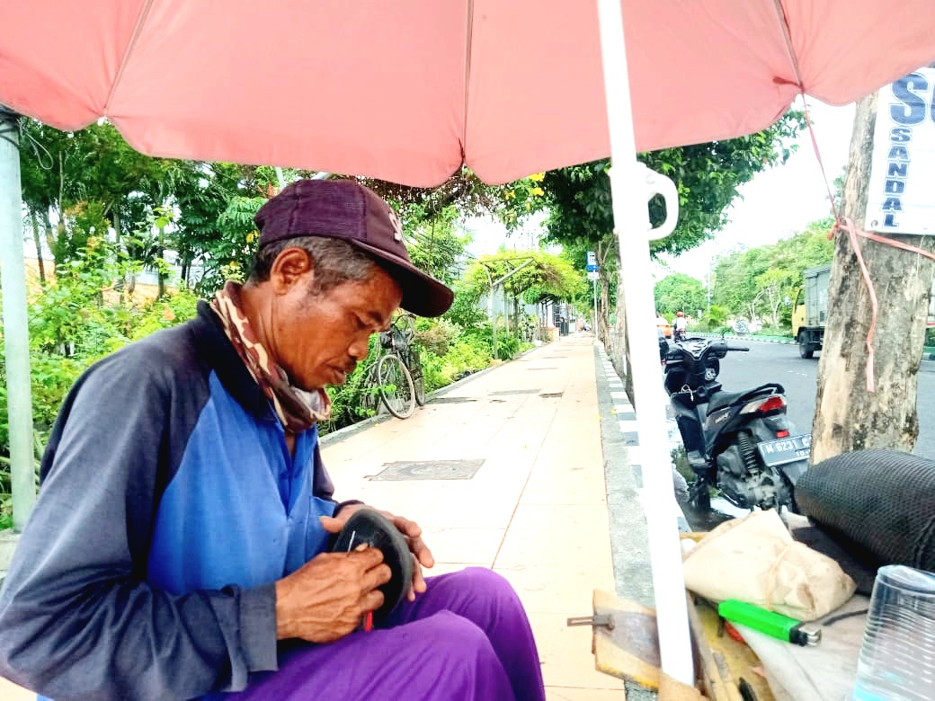 FOKUS: Suliyanto menjahit sandal milik pelanggan di tempat mangkalnya di tepi Jalan Soekarno-Hatta, Bangkalan, Jumat (6/12). (IMAMUDIN/JPRM)