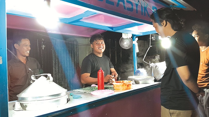MENGAIS REZEKI: Sumanto, pemilik lapak Pentol Asyik Roni di Jalan Kabupaten, Pamekasan, bersama seorang karyawannya sedang melayani pembeli, Rabu (25/12). (M. KHOLIL RAMLI/JPRM)