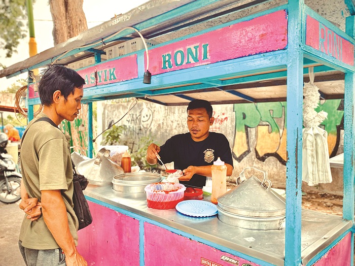 PERINTIS: Karyawan Suparmin, perintis Pentol Asyik Roni, melayani pembeli di Jalan Jokotole, Pamekasan, Rabu (25/12). (FAHMI JALIL/JPRM)