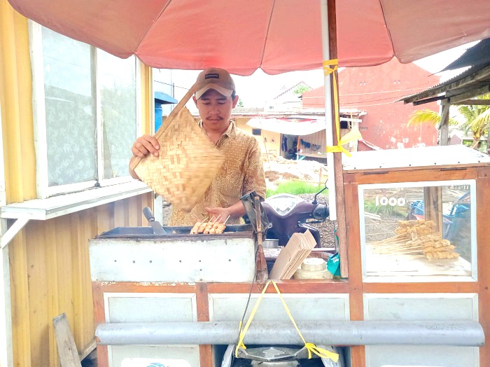 NYAMAN: Joni Pratama memproses tahu bakar pesanan pelanggan di Jalan R.E. Martadinata, Bangkalan, Sabtu (14/12). (IMAMUDIN/JPRM)