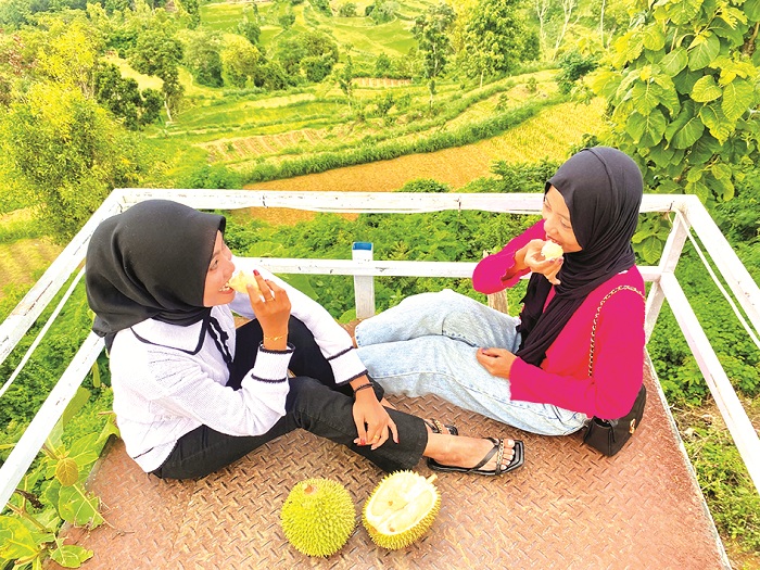 SANTAI: Nur Lailatul Qudriyah bersama Inni Mufarrofah&nbsp;menikmati durian di Wisata Puncak Ratu Pamekasan, Jumat (3/1). (MOH. IQBAL AFGANI/JPRM)