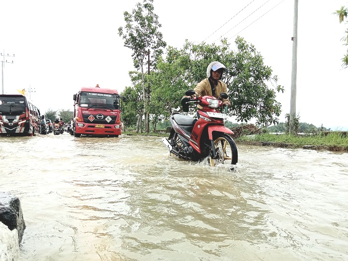 BANJIR: Seorang pengendara mendorong sepeda motornya yang mogok karena banjir di jalan nasional Desa Patean, Kecamatan Batuan, Sumenep, Rabu (22/1). (MOH. LATIF/JPRM)