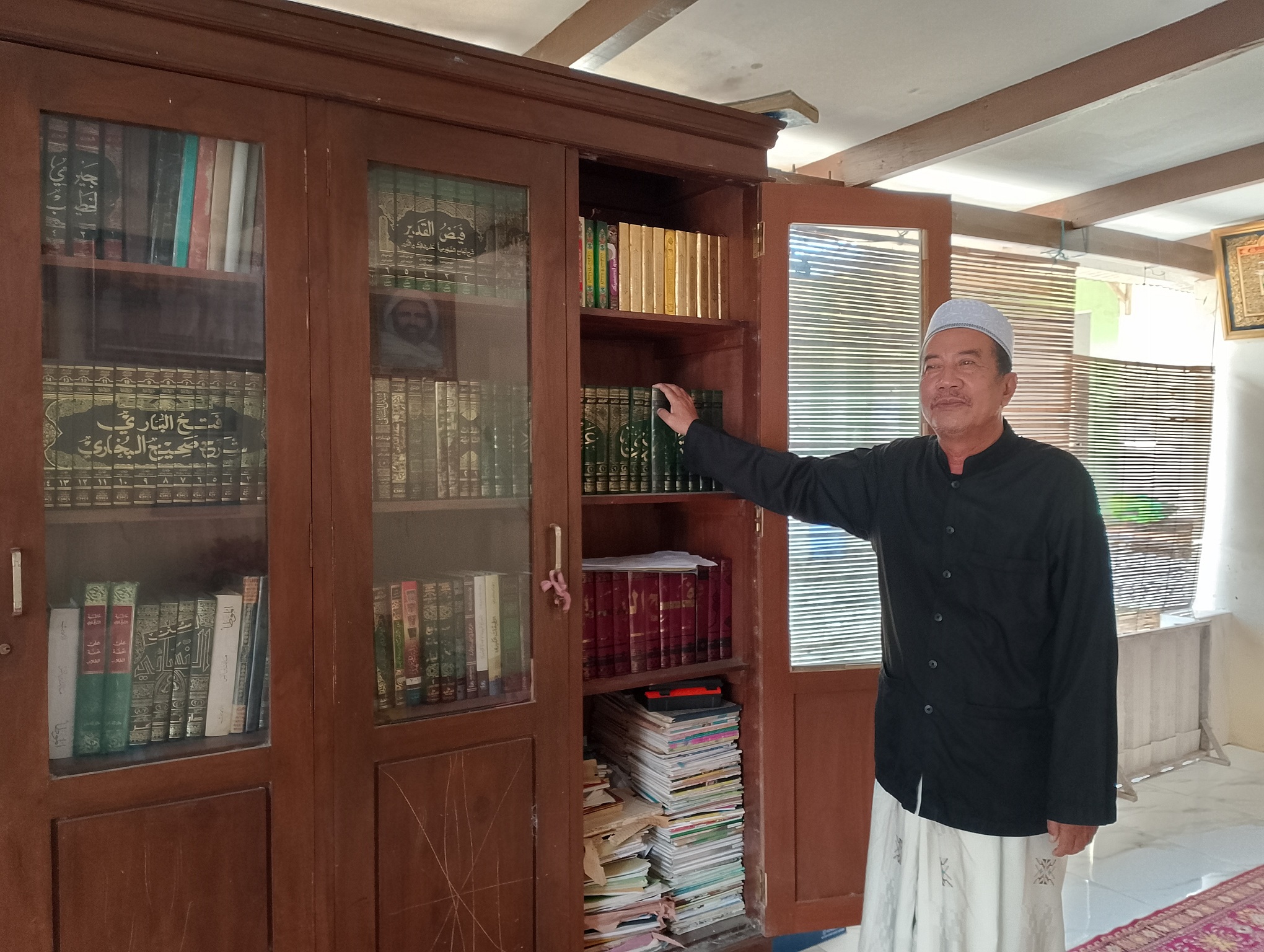 TELADAN: Ketua Yayasan Ponpes Nurul Jadid Garduak KH Ali Wahdi Dakholi mengambil kitab di rak di kediamannya, Kamis (6/3). (UBAIDILLAHIR RA&rsquo;IE/JPRM)