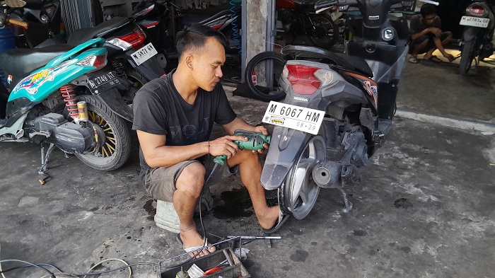 KERJA KERAS: Mawes, seorang mekanik di salah satu bengkel otomotif yang terletak di Jalan RE Martadinata Bangkalan sedang memperbaiki sepeda motor warga Kamis (12/6). (M. KHOLIL RAMLI/JPRM)