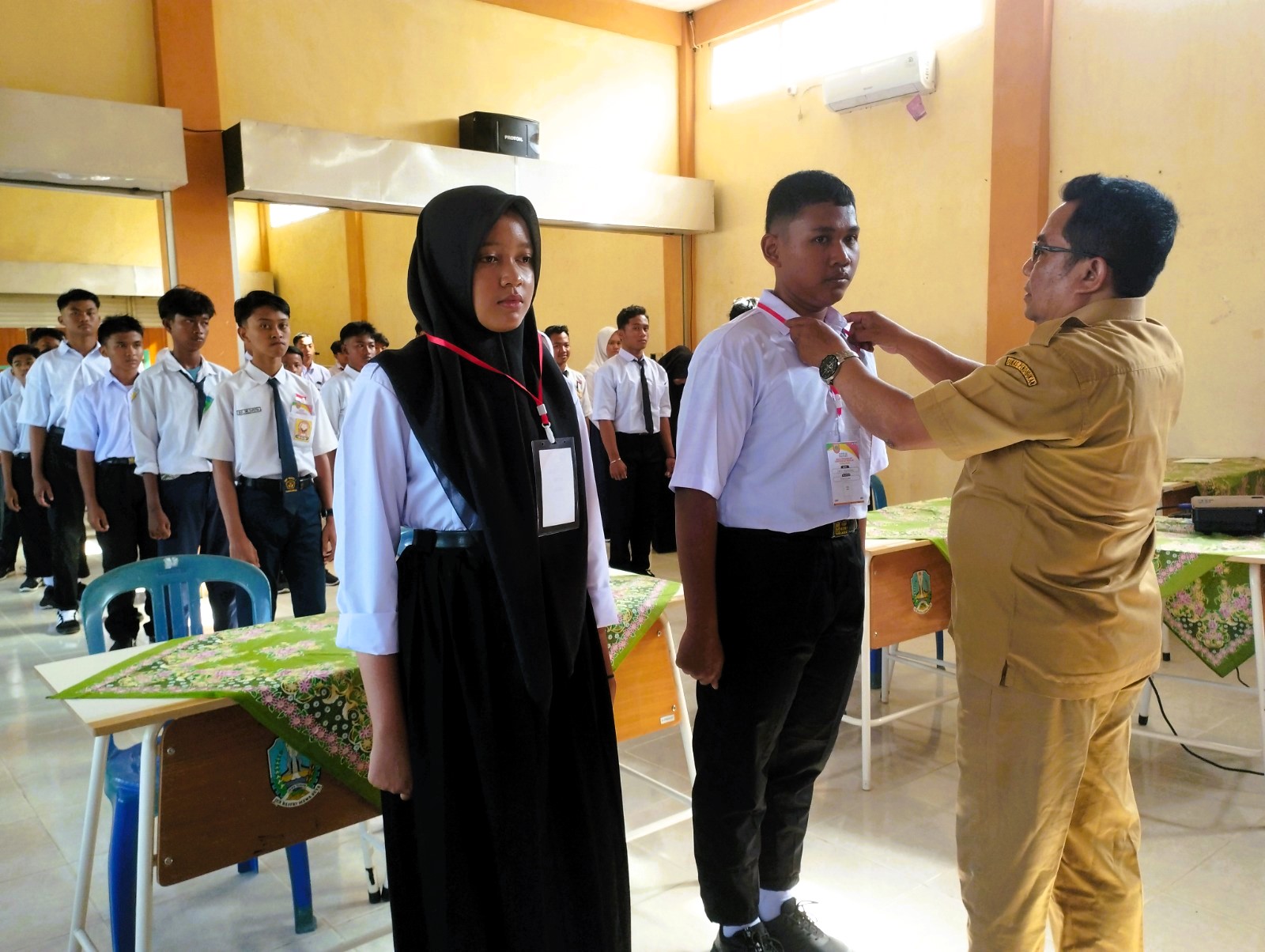 SIMBOLIS: Kepala SMK Negeri 1 Tambelangan, Sampang Suherman Hidayat (kanan) mengalungkan kartu peserta saat pembukaan MPLS, Senin (14/7).