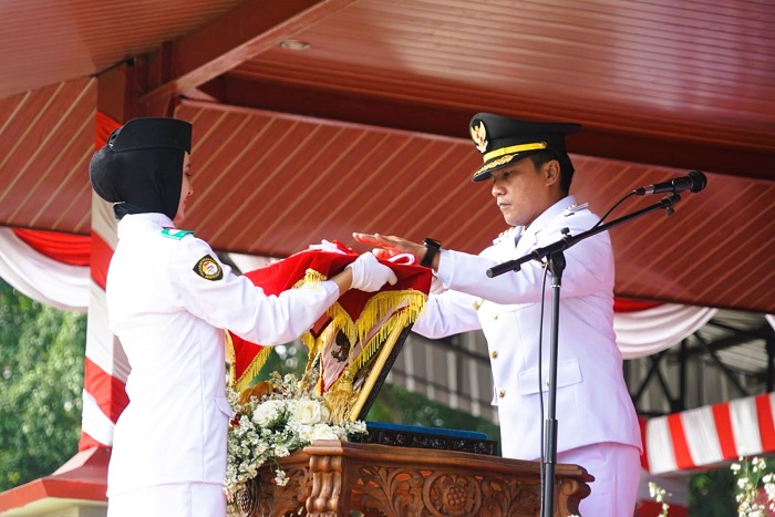 KHIDMAT: Bupati Bangkalan Lukman Hakim menyerahkan bendera Merah Putih kepada Paskibraka saat upacara HUT Ke-80 Kemerdekaan RI Minggu (17/8).
